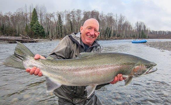 angler stood at the edge of a river holding a big steelhead/