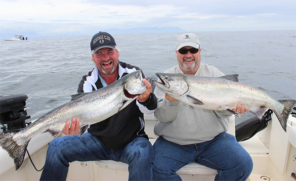 Two anglers sitting on a boat each holding a salmon caught near Tofino in Canada/
