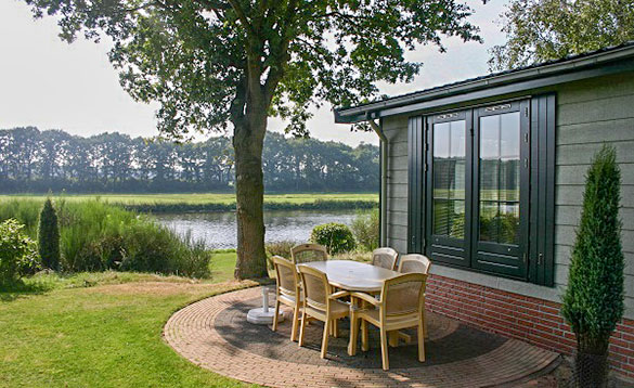 Table and six chairs on a paved patio area beside a chalet looking over to a lake at Arendshorst Resort, Holland/