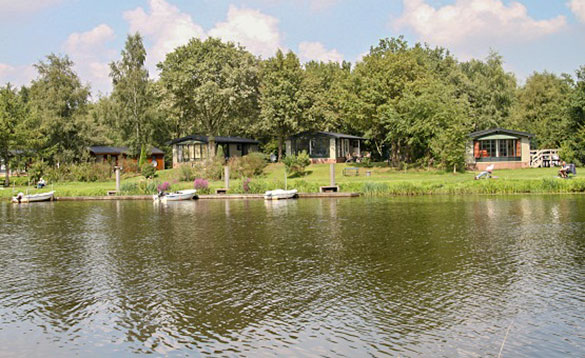 View across a lake to chalets amongst trees with rowing boats moored on the shoreline/