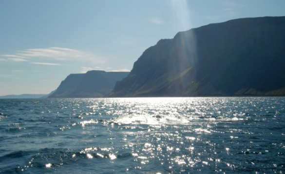 Sunlight reflecting on the waters around Iceland with hills in the background/