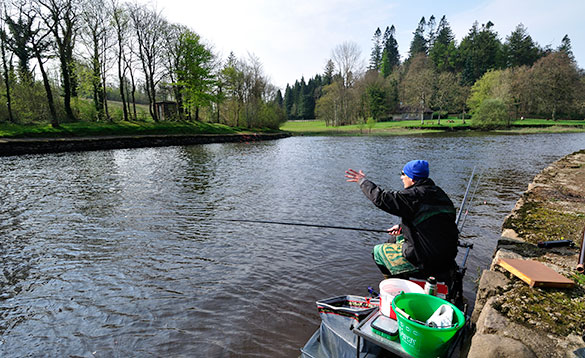angler sitting on a tackle box fishing at the edge of a river /