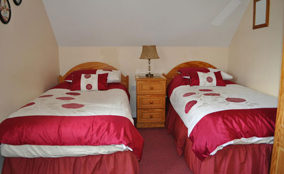 twin bedded room with pink and white bed linen and pine bedside cabinet/