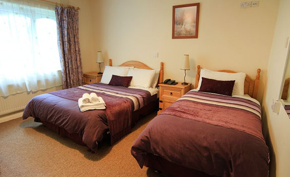 bedroom with single and double pine beds with mauve coloured bed linen /