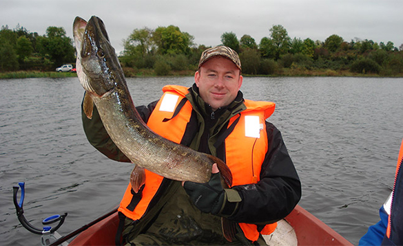 Angler sat in a boat holding a pike/