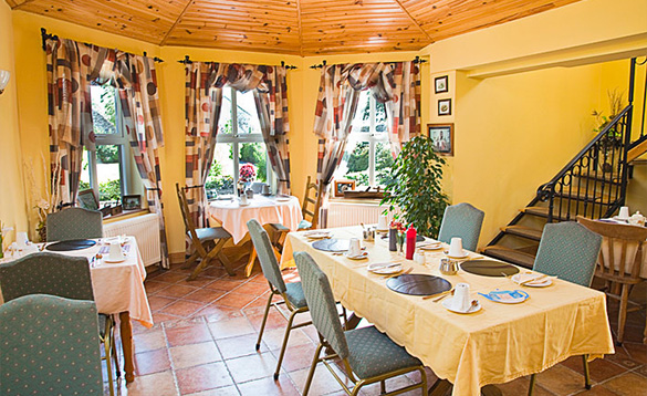 bright yellow painted dining room with tiled floor and a selection of table with yellow table cloths and chairs set for breakfast/