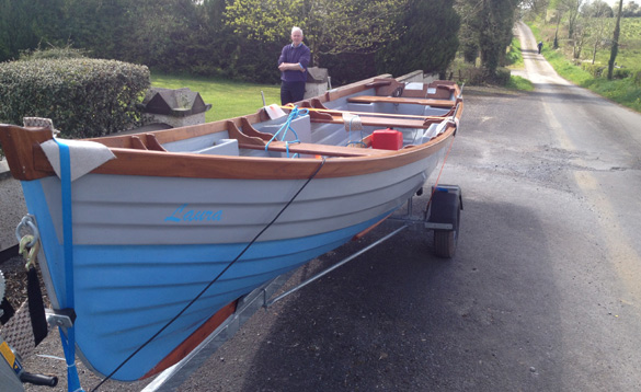 man stood beside a rowing boat on a trailer/