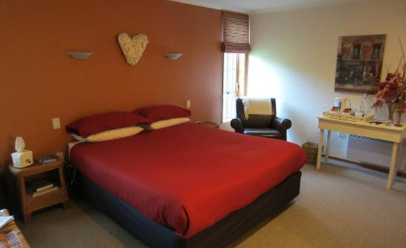 double bed with red ben linen against a dark orange wall/
