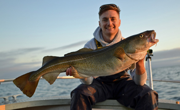 Angler sat on a boat holding a cod/