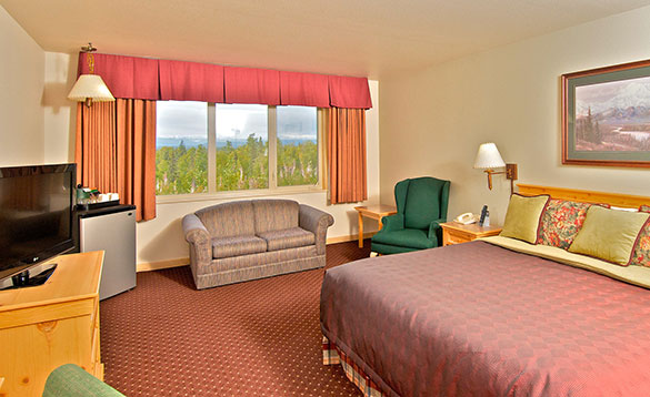 hotel bed room with large king size bed and sofa placed under the window with views of the forest and mountains/