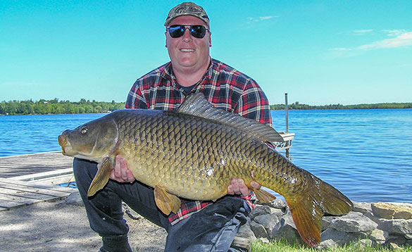 Angler stood at the edge of a lake with a large carp/