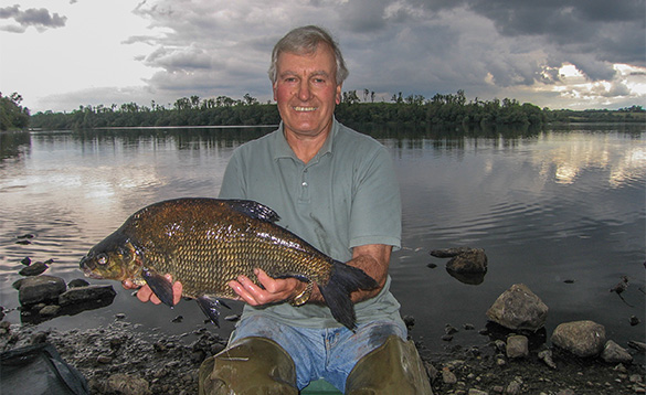 angler knelt at the edge of a river holding a bream/