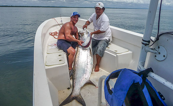 Two anglers sitting on a boat holding a large tarpon/