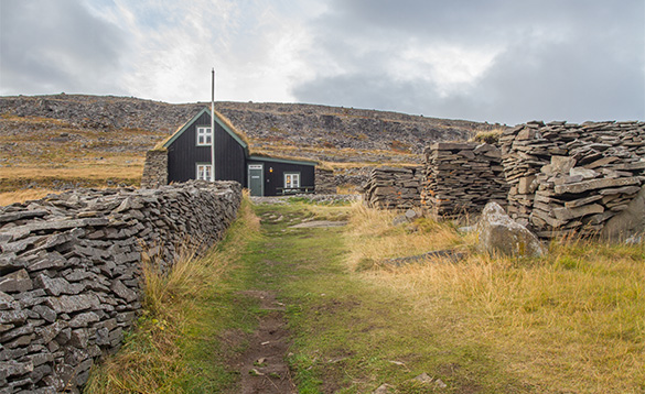 Pathway leading past stone walls to a wooden building in Iceland/