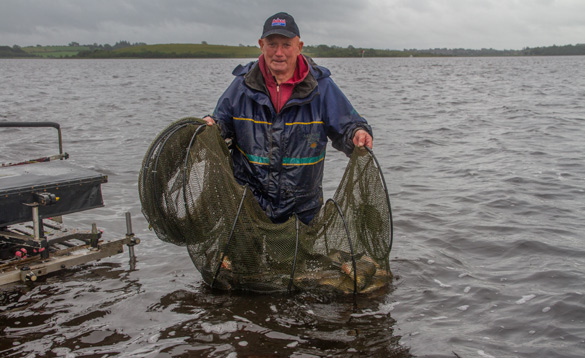 Angler stood in water with a keep net with fish in it/