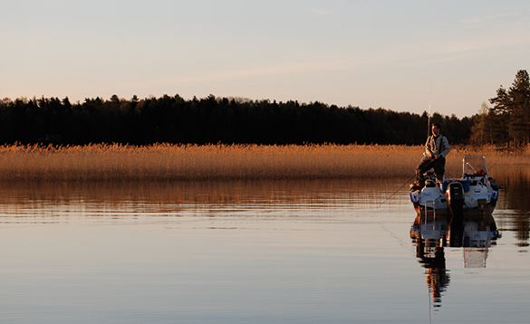 Angler standing on a boat fishing in a scenic lake in Sweden/
