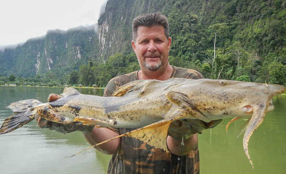 Angler standing beside a river in Thailand holding a catfish/