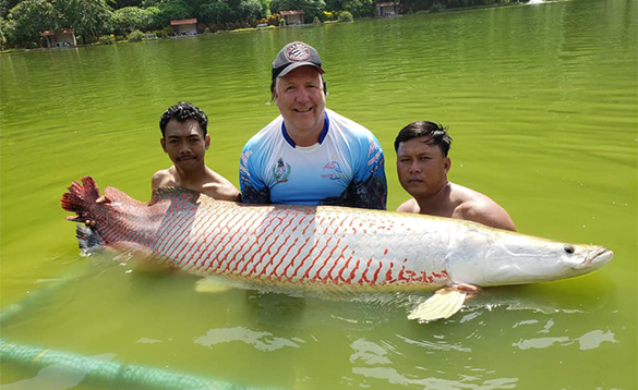 Anglers standing in water holding a arapaima fish/
