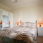 Bedroom with white wardrobes with mirrored doors, two white bedside cabinets with lit lights either side of double bed with brown patterned bedding