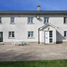 White plastic table and six chairs in front of a large white two storey house with grey slate roof