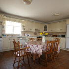 Table with red and white patterend table cloth and six pine chairs in a cream coloured kitchen