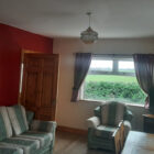 Green and white striped setttee and chair in a living room with red feature wall