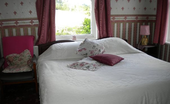 Double bed with white bed linen and one red cusion and two pink flower patterned cushions on it