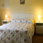Two lamps lit on two white bedside cabinets either side of a double bed with white quilt with pink flower pattern