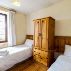 Bedroom with double and single bed with white quilts and pine wardrobe