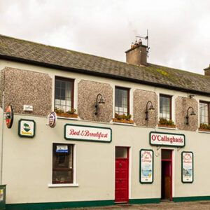 Two storey Irish pub with cream painted lower half with red door and four lights between the upper room windows