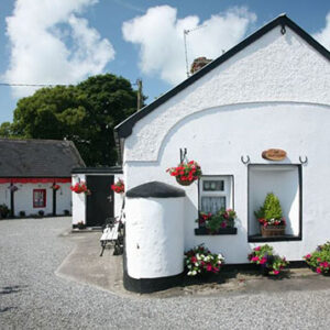 Two cottages painted white with hanging baskets pots and window boxes full of colourful flowers