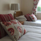 Two single beds with white quilts and red striped pillow and cushions with poppy flowers on them
