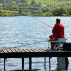 Man in red coat fishing from wooden jetty