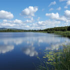 White clouds reflected in a lake surrounded by trees with hills in the background