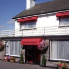 White two storey building with hanging baskets and pots full with multicoloured flowers