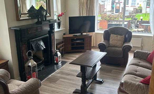 Lounge in self-catering property with feature open fireplace and fawn three piece suite around a dark wood coffee table