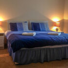 Two lit bedside lamps on cabinets either side of double bed with blue striped linen