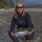 Lady knelt beside a river holding a coho salmon