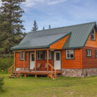 Orange painted log cabin with green roof and stairs leading to a porch