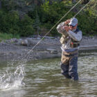 Angler fly fishing in a river as a hooked fish splashes in the water