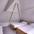 Three pine single beds with white bed linen in converted loft bedroom