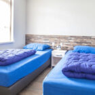 Bedroom with two single beds with dark blue bed linen and small white bedside cabinet between the two beds