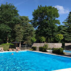 People on sun lounges around a swimming pool with two people swimming in it