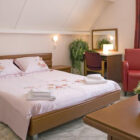 Bedroom with double bed and pink linen with flowers on it and red leather chair beside a window