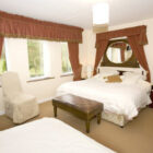 Formal bedroom with a large double bed, heavy burgundy curtains with gold fringe, a leather bench, and an ornate mirror headboard.