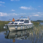 Three people on deck on a white cruiser navigating through rushes on a river