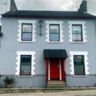 Large grey two storey terraced house with steps leading to a porch and red front door