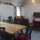 Open-plan living and dining area with a long wooden table, black cross-back chairs, and red upholstered armchairs on decorative geometric floor tiles.