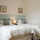 Bedroom with two single beds with blue painted headboards, white linen cream throws and blue patterned cushions