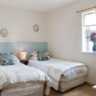 Bedroom with two single beds with blue painted headboards, white linen cream throws and blue patterned cushions